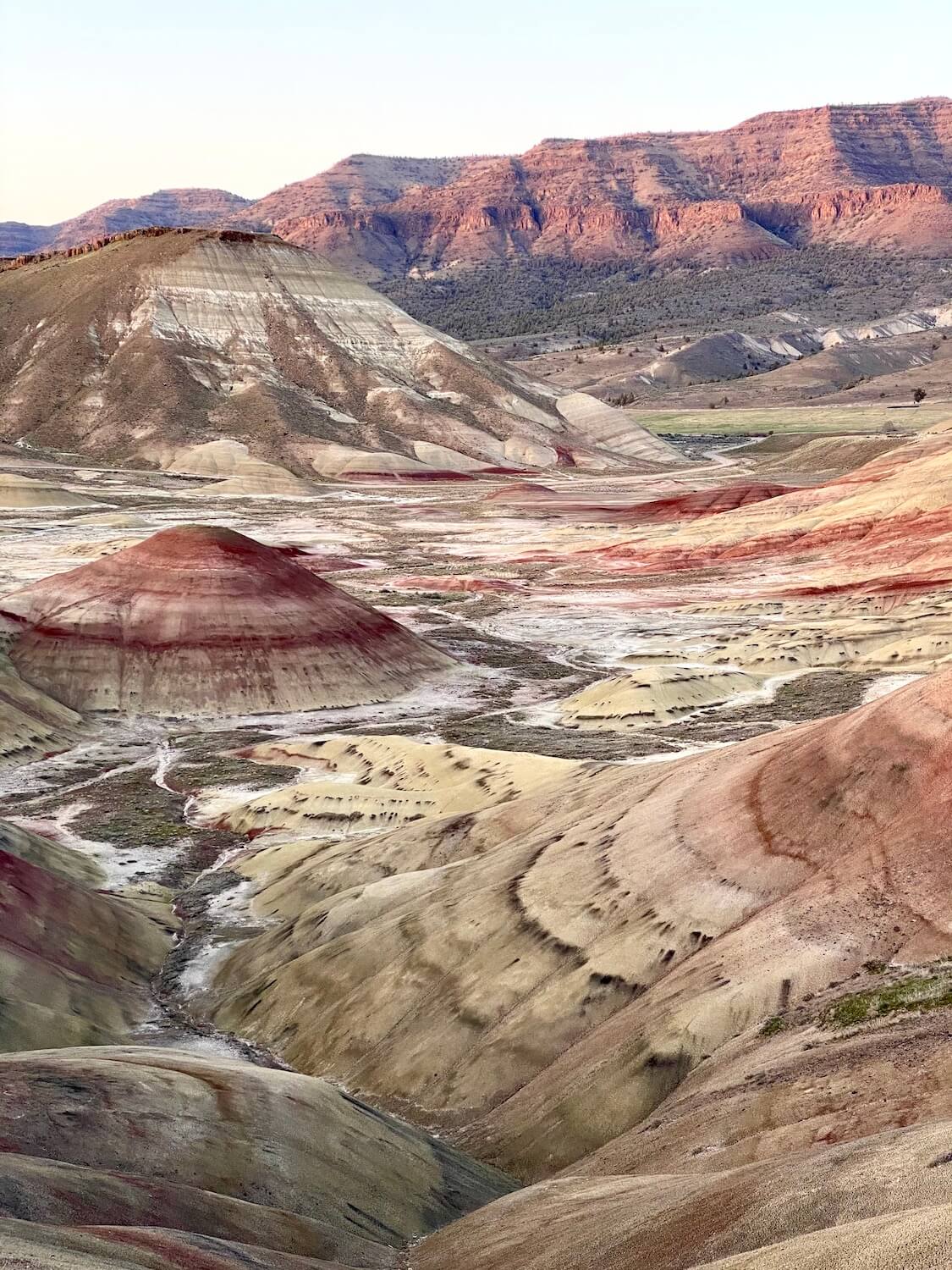 This is one of the highlights in the collection of Painted Hills Oregon photos.  The landscape feels like the moon, with bubbling red mounds that meet a valley floor covered in the white chalky substance.  The sunset shines on the ridge high above in the distance.  