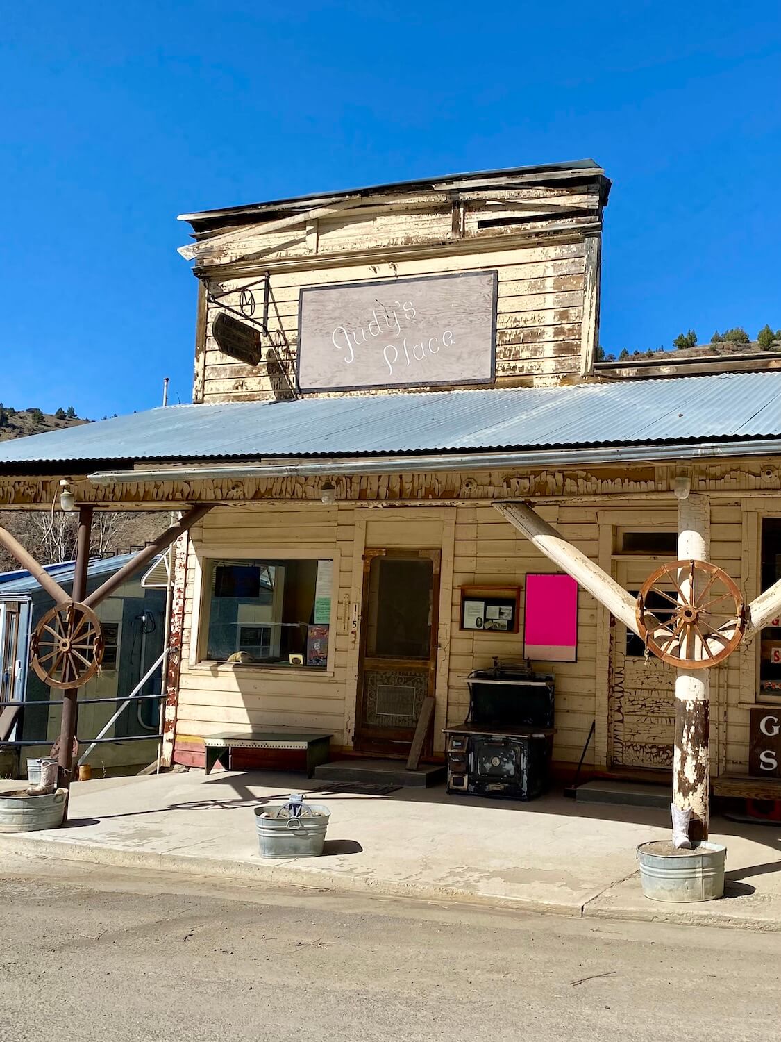 An antique store in Mitchell, Oregon named Judy's Place shows off a western style store front that could be from the pioneer days.  Two old wagon wheels are propped up on the support beams and a bright pink sign is posted near the door. 