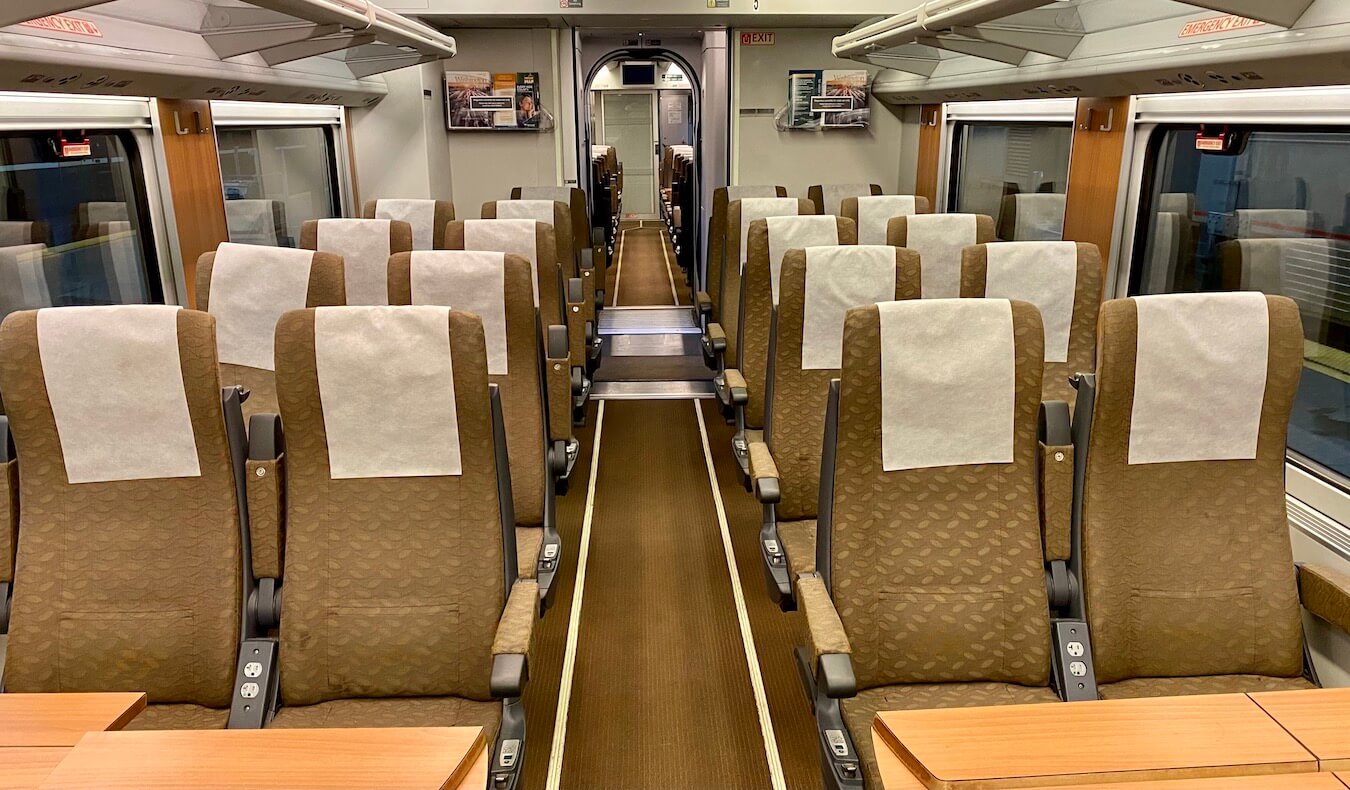 Coach class seats are four abreast on the Amtrak Cascades train from Seattle to Vancouver. The seats have white fabric covers near the headrest and are otherwise a brownish tan color.