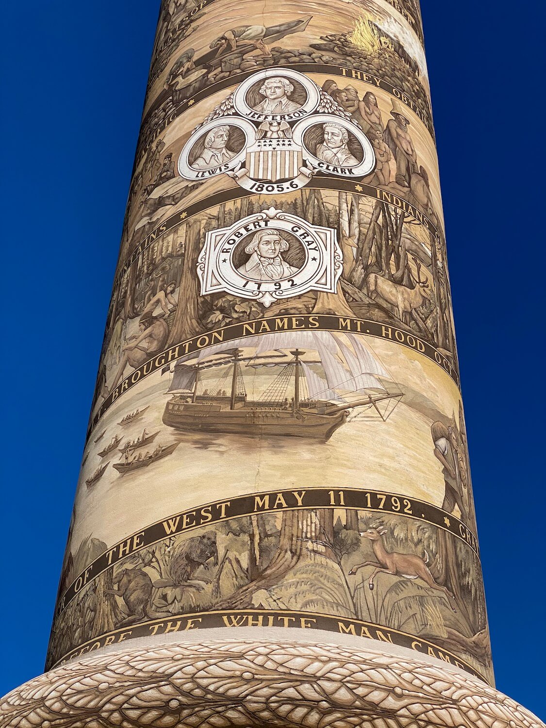 A section of the Astoria Column has intricate information painted onto the stucco surface.  The sky is a vibrant blue in the background.