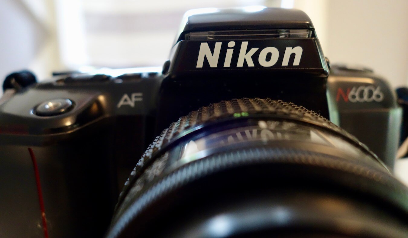 The Photo Gallery of Kessi World has many past cameras, including this Nikon N6006 SLR film camera from the late 1990's.  The NIKON letters are prominent in the shot, with black casing and features. 