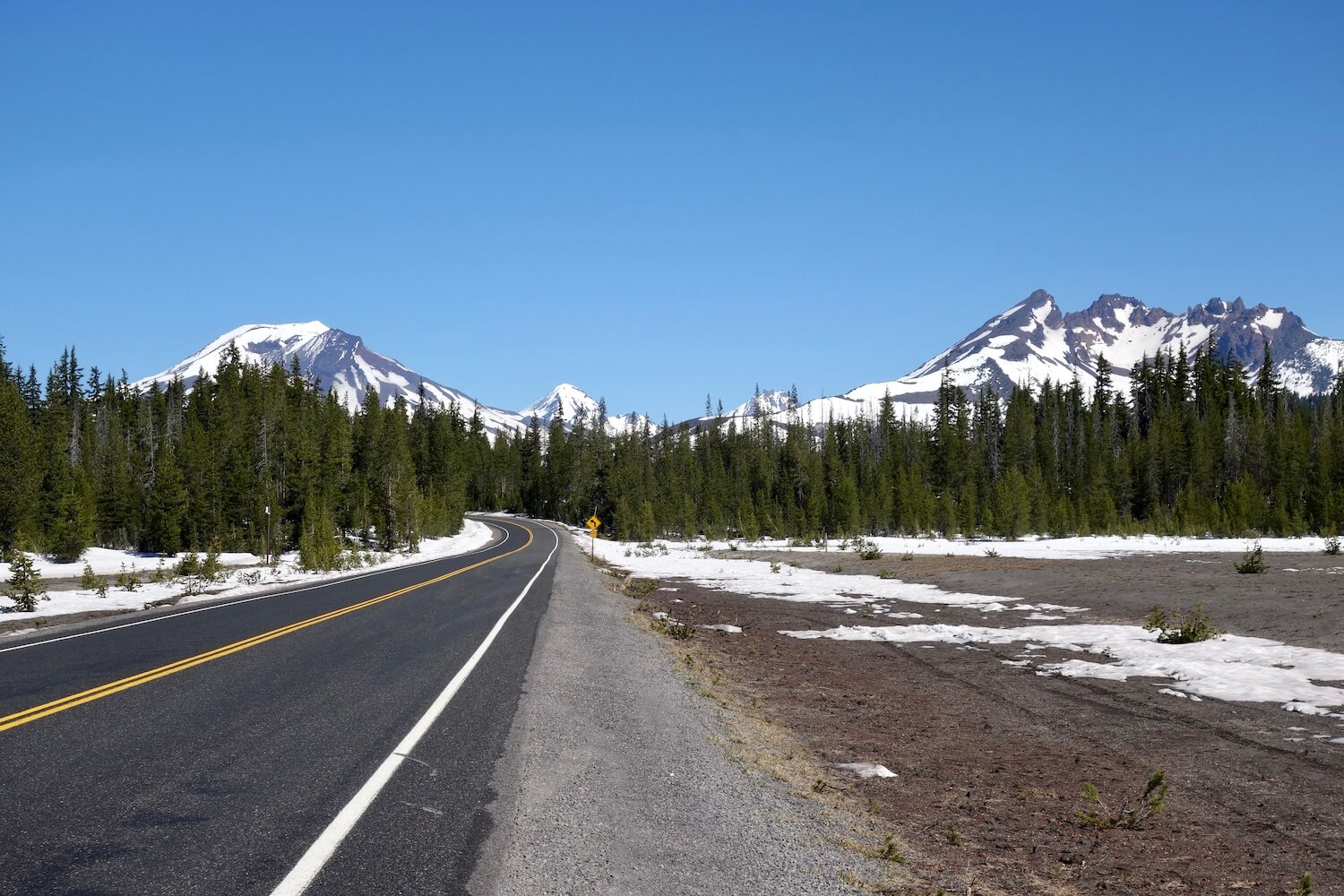 This Oregon road trip stops amongst the Cascade Mountains which are still snow covered in this photo.  There is also snow along side the road. 