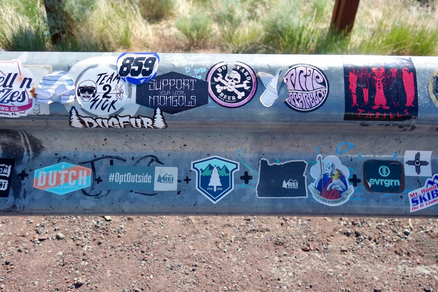 An up close shot of a highway guardrail covered in stickers that show different places in Oregon.  