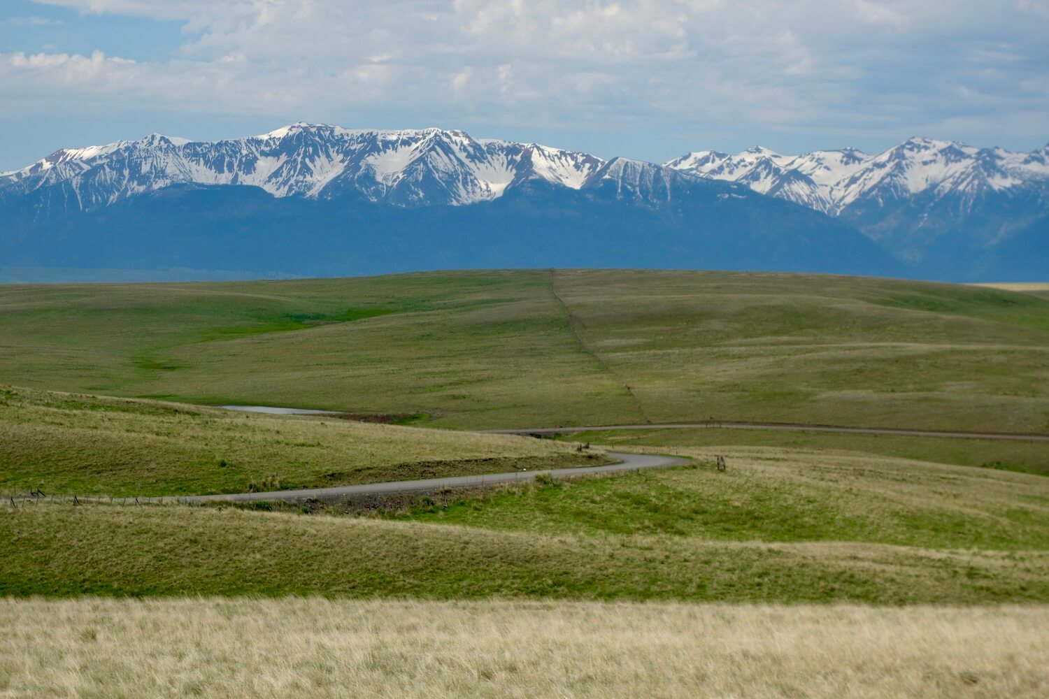 This photo taken on an Oregon road trip shows a winding gravel road leading toward the majestic Wallowa Mountains that are still snow capped in the background. 
