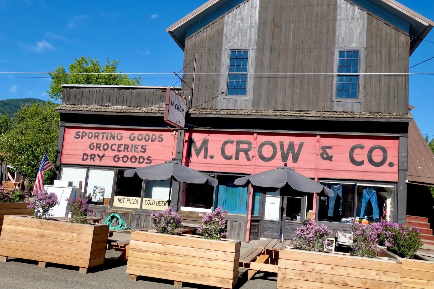 A mercantile along the side of the road on a trip through Oregon has a pink sign that says M Crow and the side of the building is painted brown wood.  