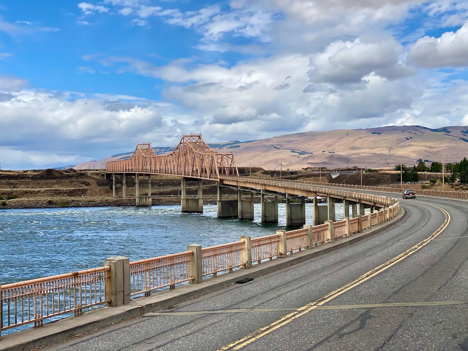 The Dalles Bridge leads from Oregon to Washington State and the pinkish metal structure crosses the Columbia River after making a curve.  