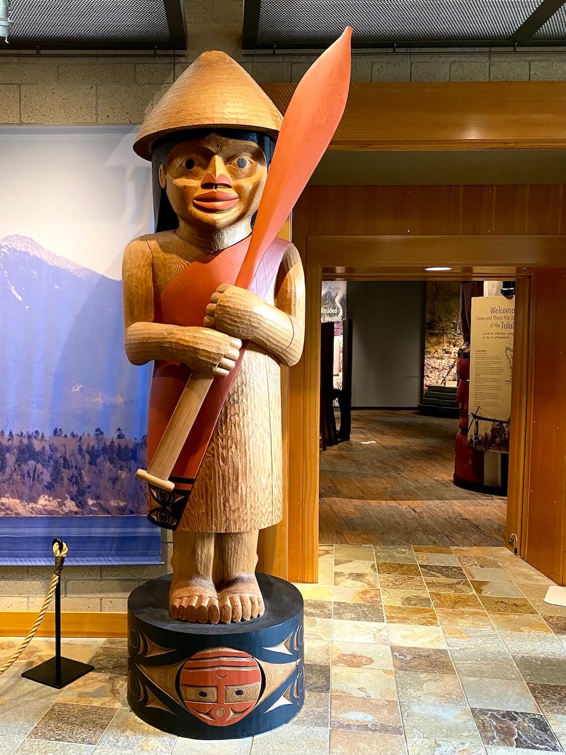 A carving from a cedar tree made into a Salish boater carrying a paddle adorns the entrance to the Hibulb Cultural Center.  Inside the two doors leading to the exhibits there are lights shining on placards with information. 