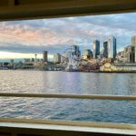 The Seattle waterfront seen through a metal opening in a Washington State Ferry. The water reflects the pinkish glow of the sunset sky.