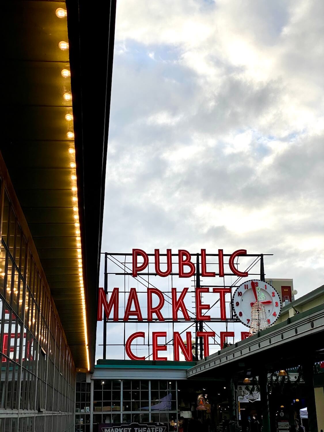 View of Pike Place Market in Seattle under Winter light.  The red neon letters say Market Center and the large clock shows almost 3PM.