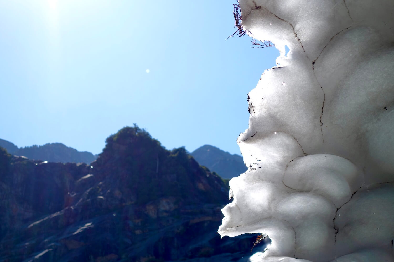 A close up of the ice forming the ceiling of the cave at Big Four Ice Caves. The lines of the ceiling are made by faint dust and pine needles as the sun shines high above in the blue sky.