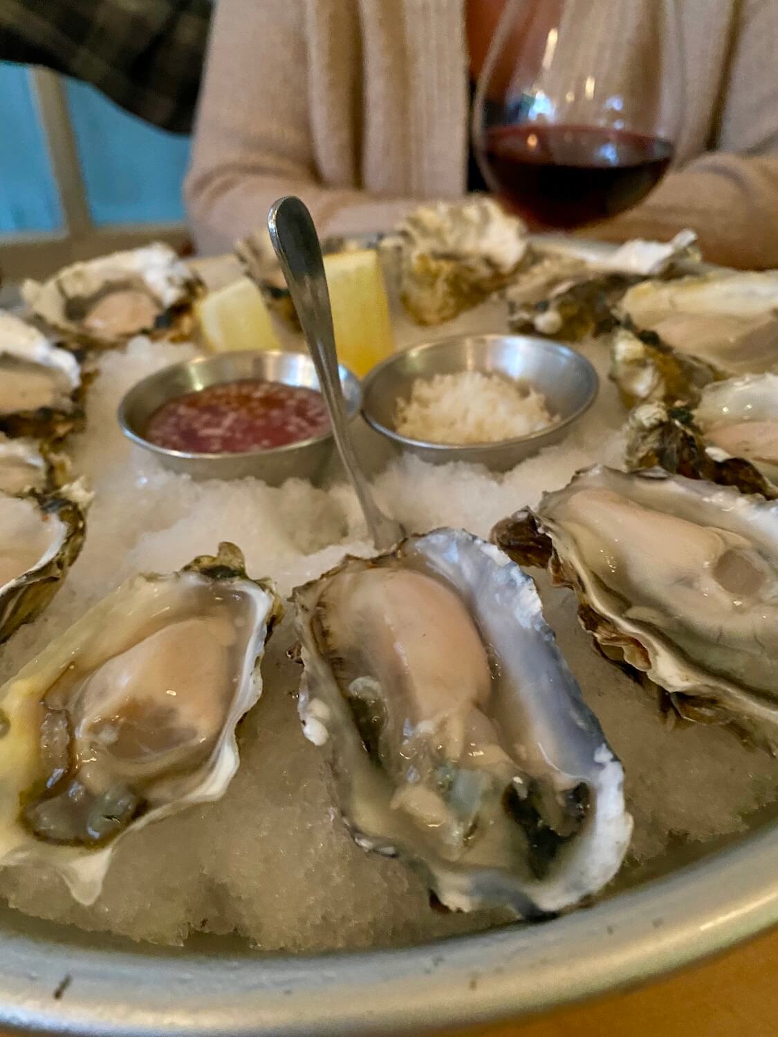 Fresh raw oysters are loaded onto a tray and packed with ice at Finistere Restaurant in Port Townsend, Washington. In the background someone is drinking a glass of red wine.