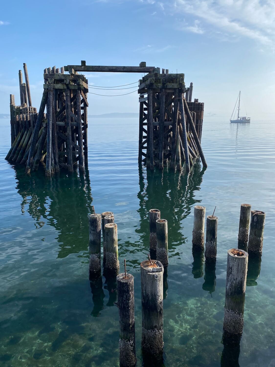A ferry dock landing sits empty while several old log pilings pop up from the clear waters of the Salish Sea.