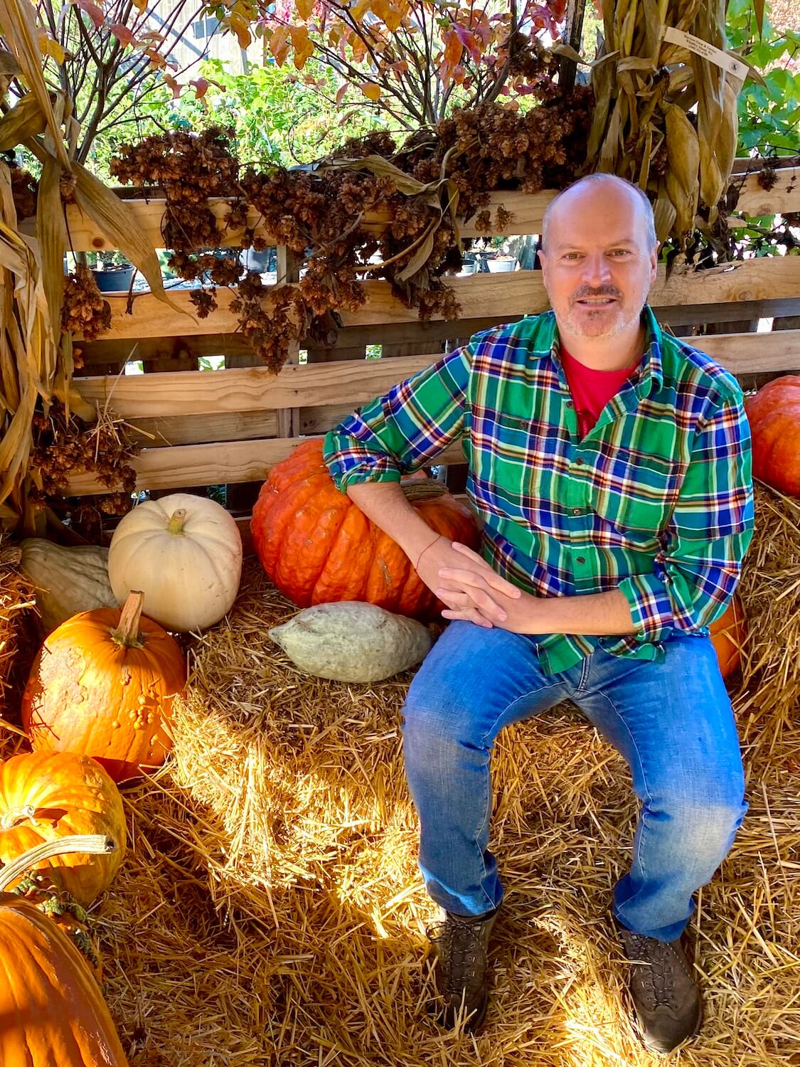 Matthew Kessi sits on a bale of straw for this photo of a fall harvest scene, complete with pumpkins and gourds and corn stalks tied to a wooden fence.
