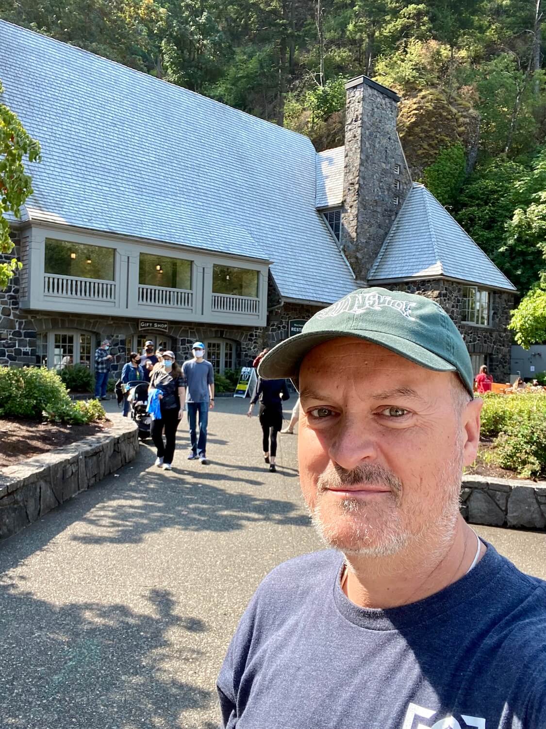 Matthew Kessi takes a selfie at Mulnomah Falls Lodge. There are people coming out of the lodge, which has a large stone fireplace and sweeping shake roofline.