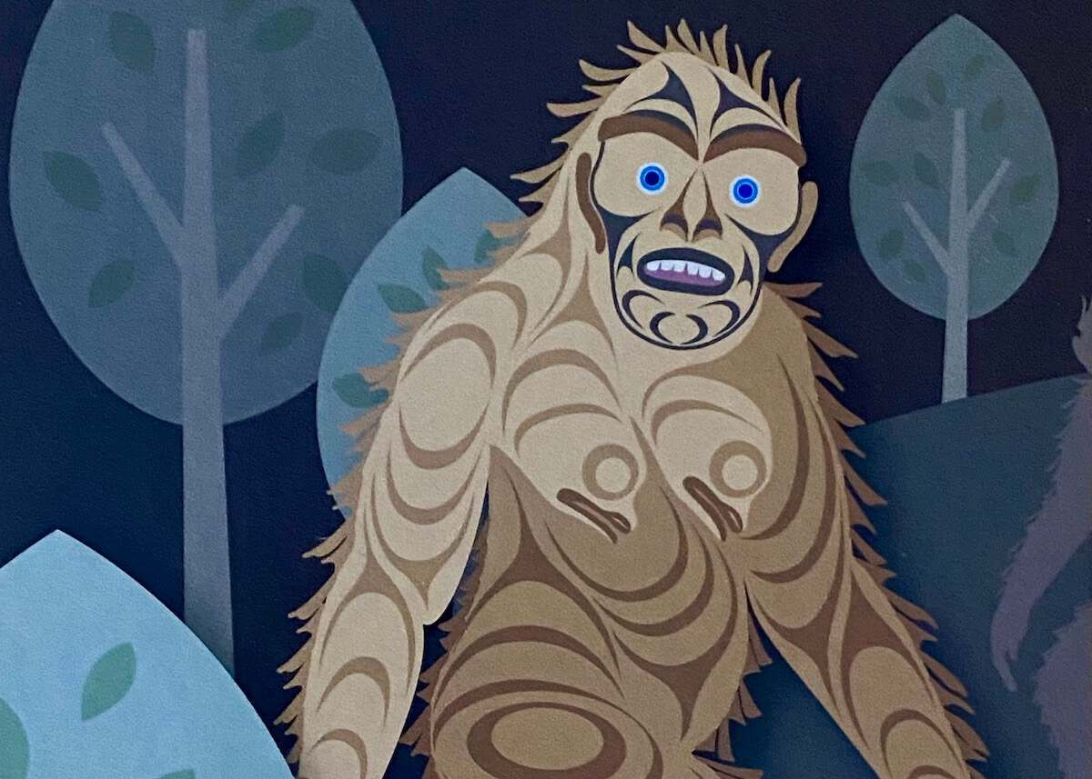 A drawing of Sasquatch from a Coast Salish artist depicts him walking in the forest with rounded trees. He has piercing blue eyes and purple mouth with black drawn in features around his face. The rest of him is different swirls of browns depicting fur.