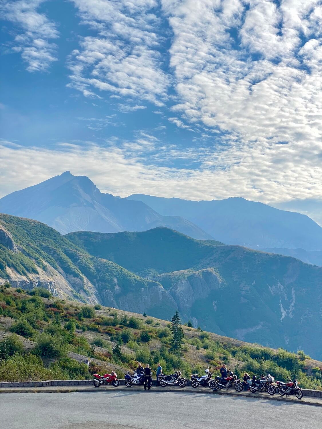 The different layers of Mount St. Helens as seen from the Windy Ridge Viewpoint. In this photo there is a group of motorcycle riders parked along the viewpoint taking in the view. 