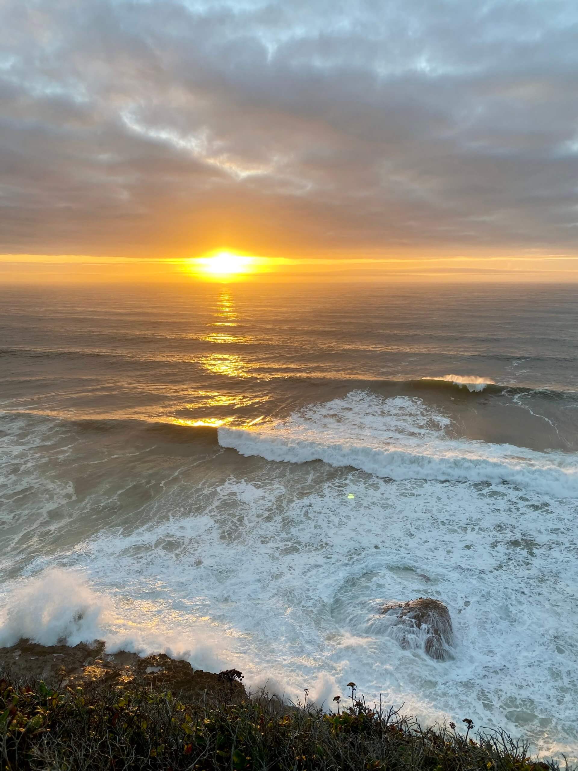 Sunset photo taken near Yachats, Oregon casts a buttery yellow glow over the Pacific Ocean as waves crash onto rocks and create a foamy white suds.