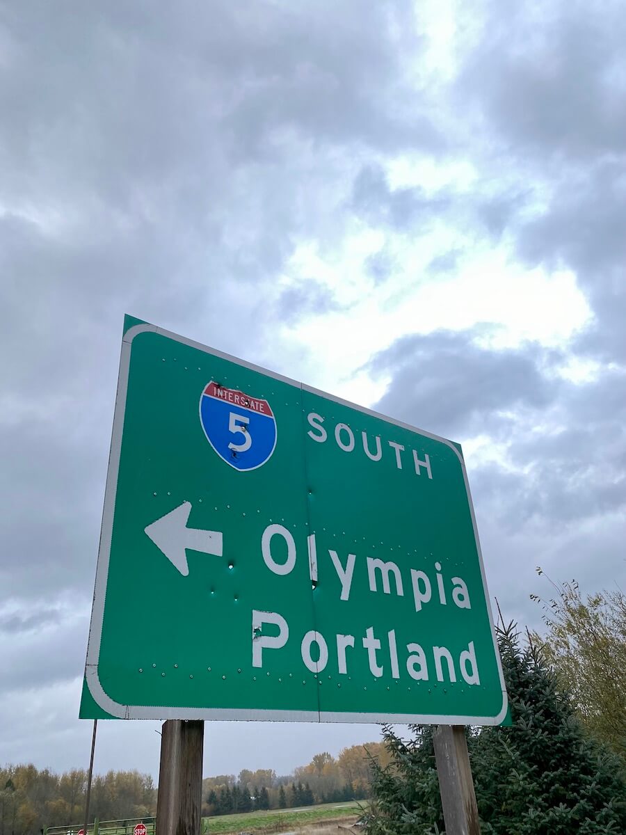 A road sign on Interstate 5 directs drivers to Olympia and Portland. The clouds are gray in the background.