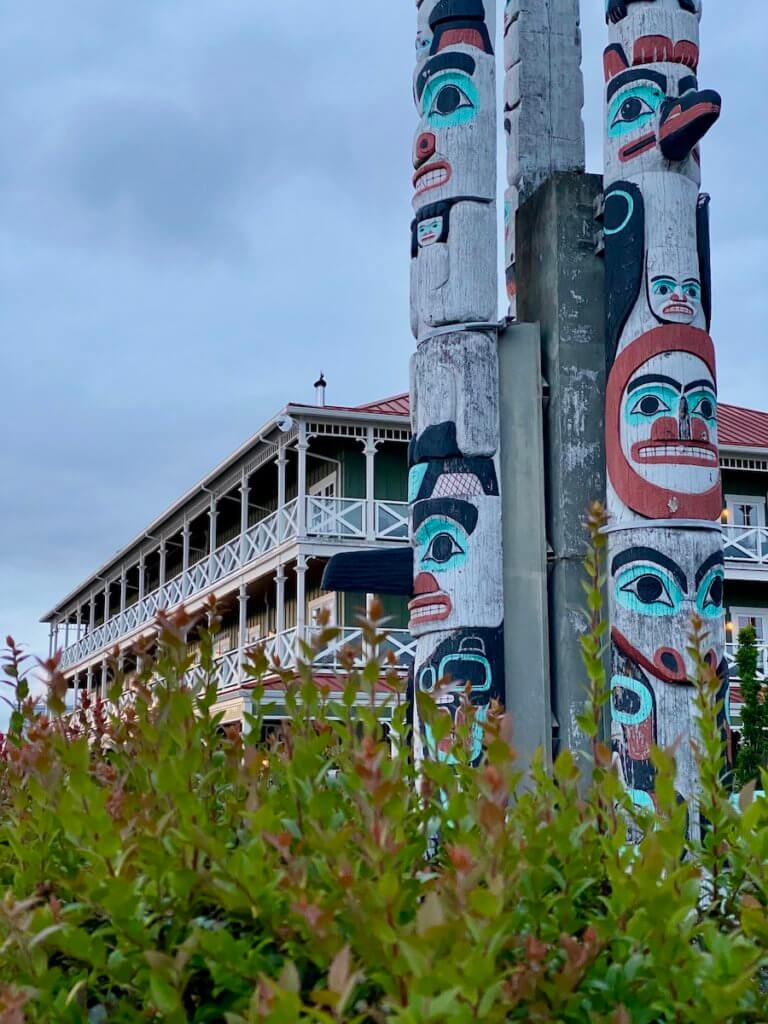 Native totems line up next to each other with red, aqua and black paintings while the McMenamins Kalama Harbor Lodge takes the scene in the background.