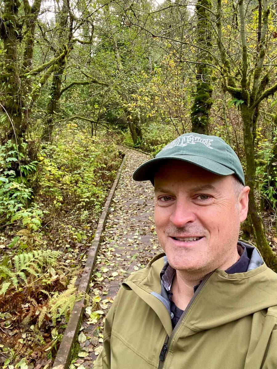 Matthew Kessi poses for a selfie on a boardwalk along the drive between Seattle and Portland. He's smiling while wearing a green cap.