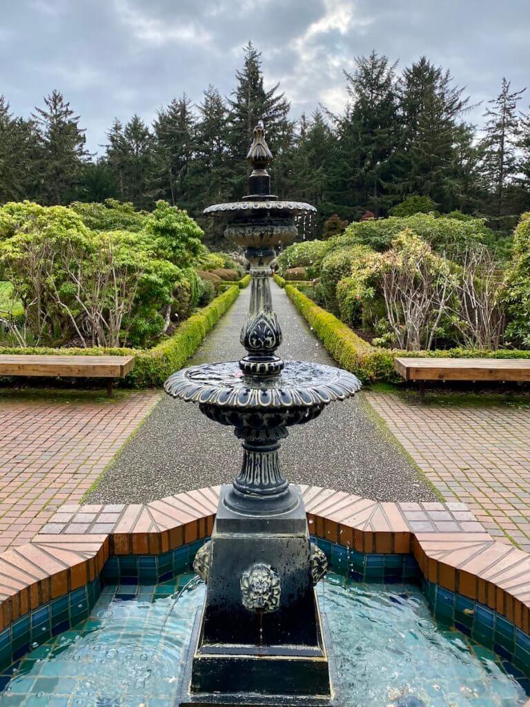 An ornate fountain drips water in the middle of a formal looking botanical garden on the Oregon Coast.