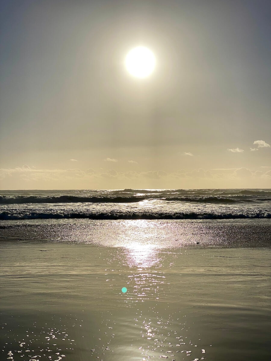 A lazy yellow sun hovers over the Pacific Ocean and shines a glow on the rolling surf and glistening sand on the beach.