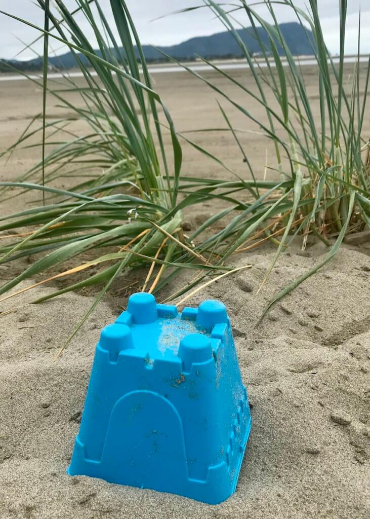 A plastic blue sand castle mold sits in the sand near two bunches of seagrass on a beach along the soulful Oregon Coast, near Seaside.