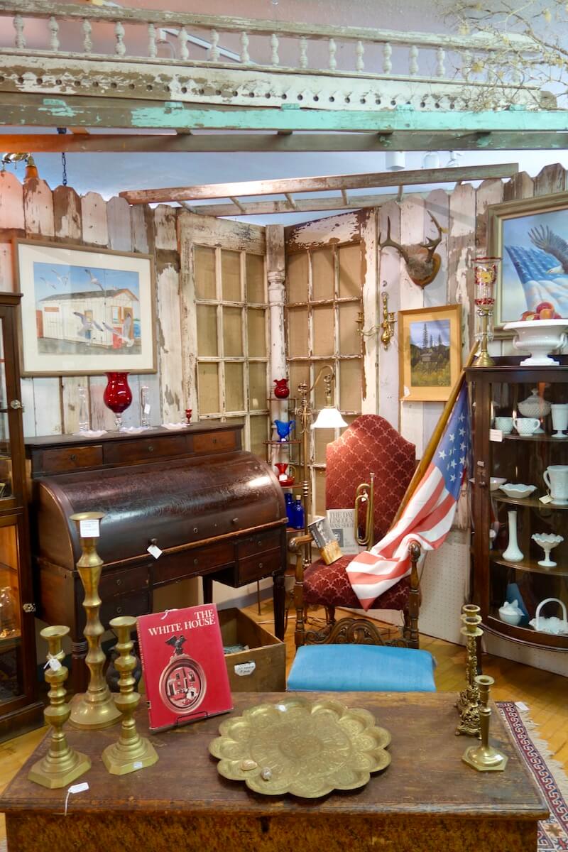 A corner of an antique store shows off different items for sale, such as an American flag and a hutch.