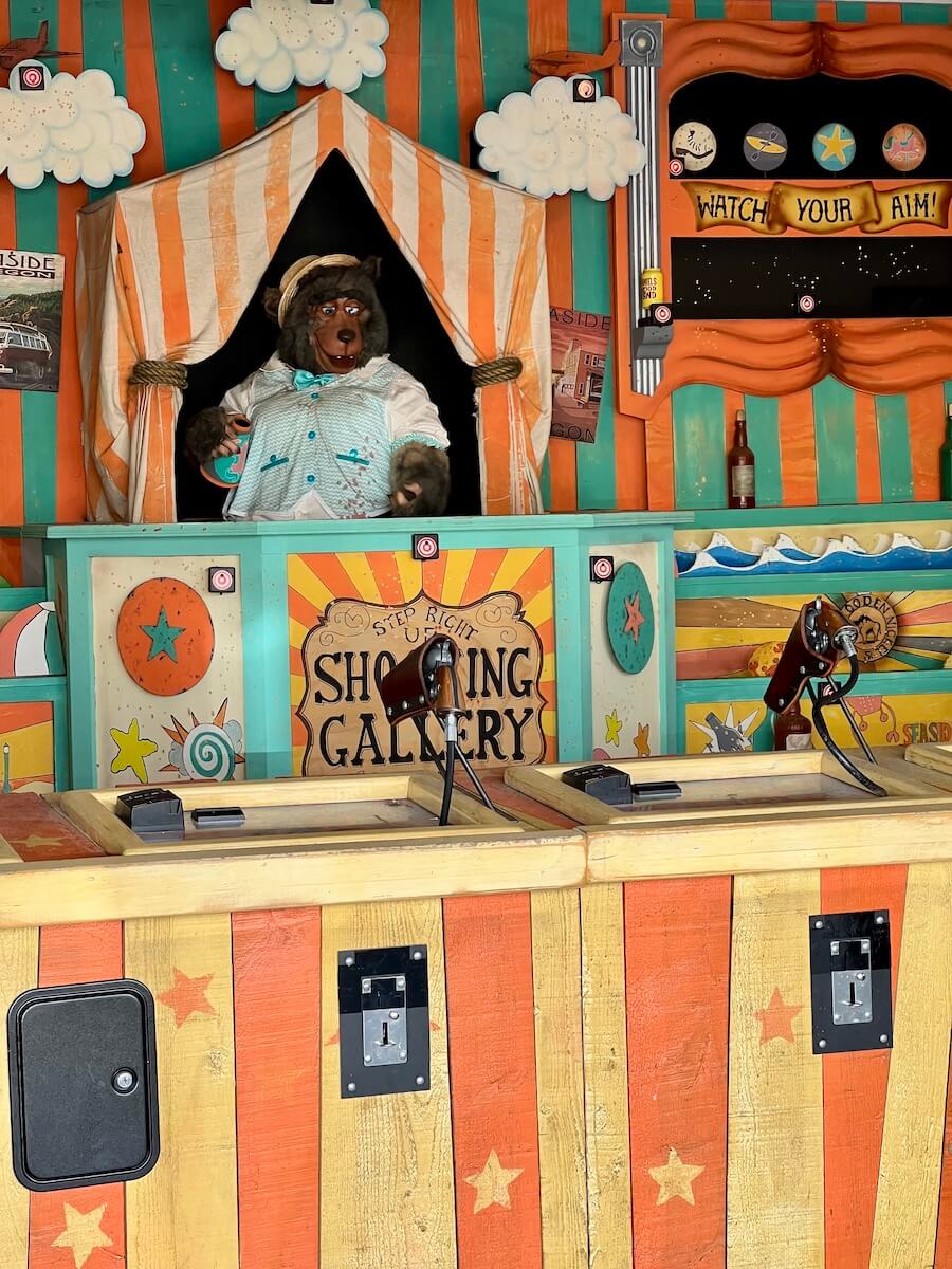 It can be fun to play carnival games in Seaside Oregon. This is a shooting gallery with orange and yellow striped wood enticing people to come join. A stuffed bear is in an opening to the back of the shop.