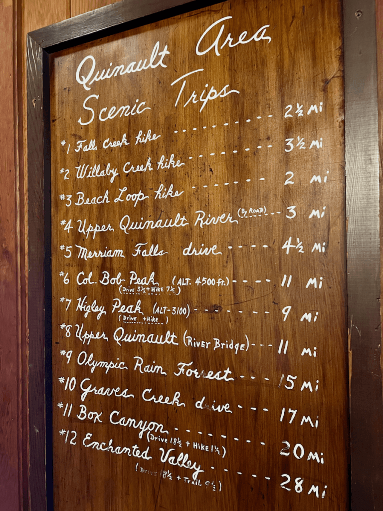 A menu of trails available from Lake Quinault Lodge is written with white ink on a polished wood slate. The title says Quinault Area Scenic Trips.