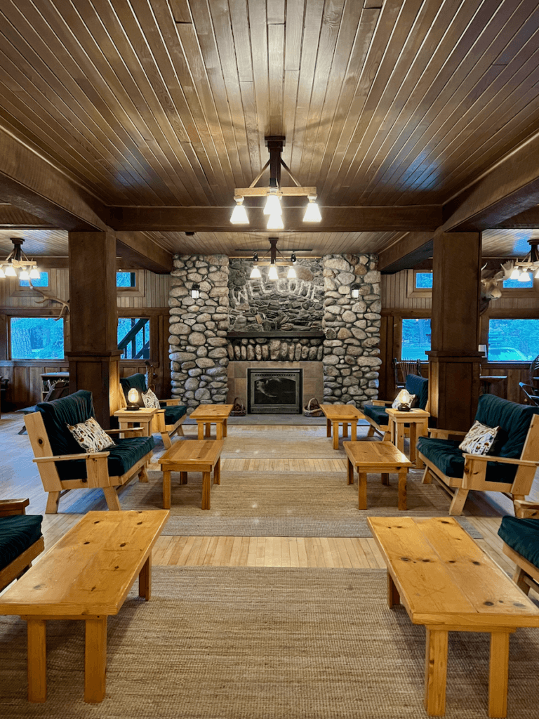 The grand lobby of the Wallowa Lake Lodge is cozy with furniture made from yellow pine and green cushions. The fireplace in the background is made from river stone and etched above the fire it says "Welcome"