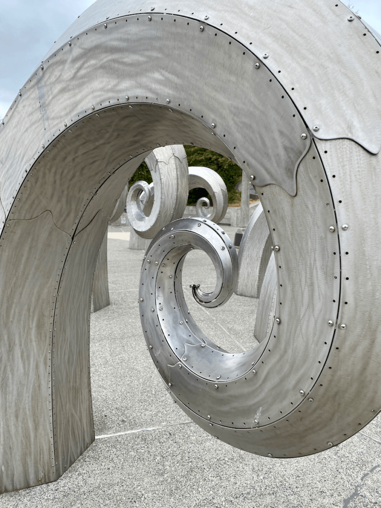This art sculpture has titanium pieces of metal riveted together to form spirals on top of concrete.