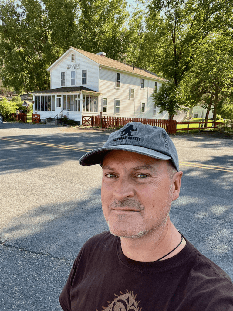 Matthew Kessi poses for a selfie in front of the Frenchglen Hotel in Eastern Oregon. This hidden hotel is only available by calling for rates. The historic looking building is painted cream color and is situated under voluminous cottonwood trees.