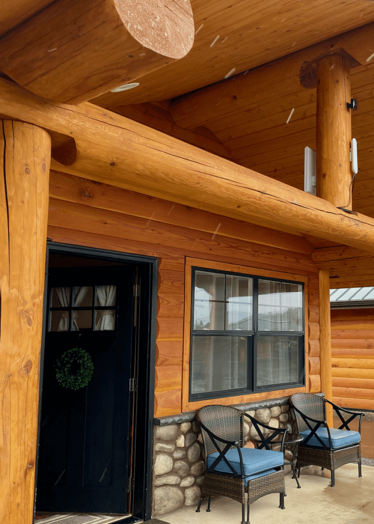 Rain pours in front of a lodge room in Forks, Washington made for lacquered fir. There is a front door and two wicker chairs on a patio under the awning.