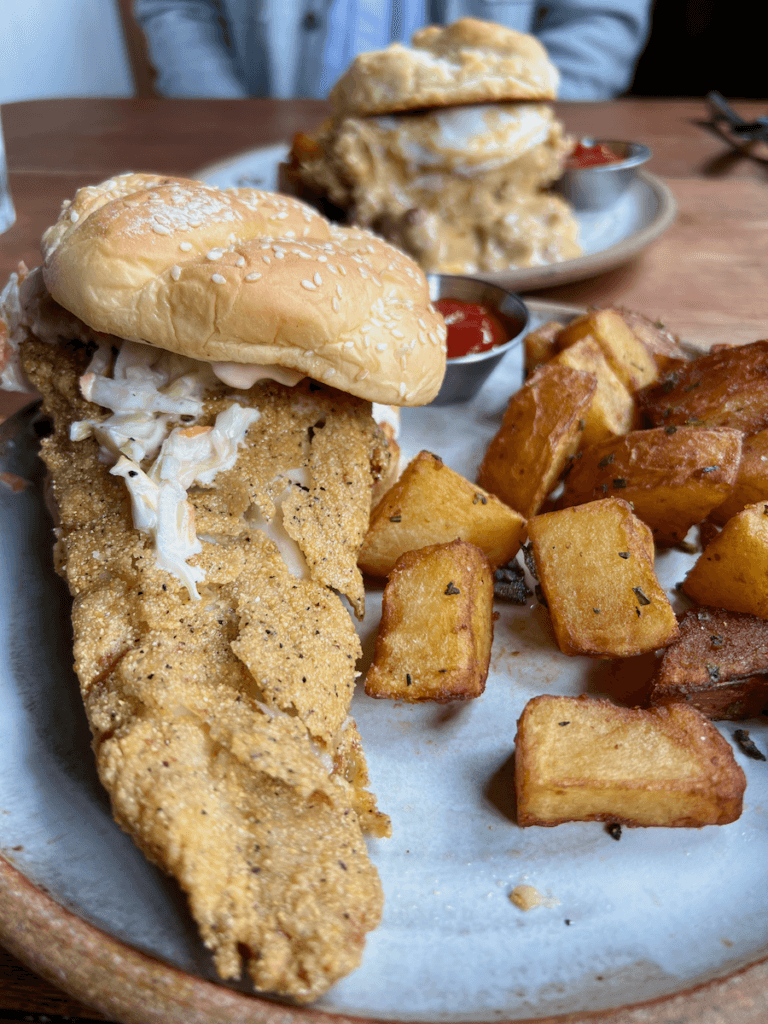 A delicious fish sandwich is paired with home fries in the dining room of Tokeland Hotel on the Washington Coast. There is a chicken sandwich in the distance as well.