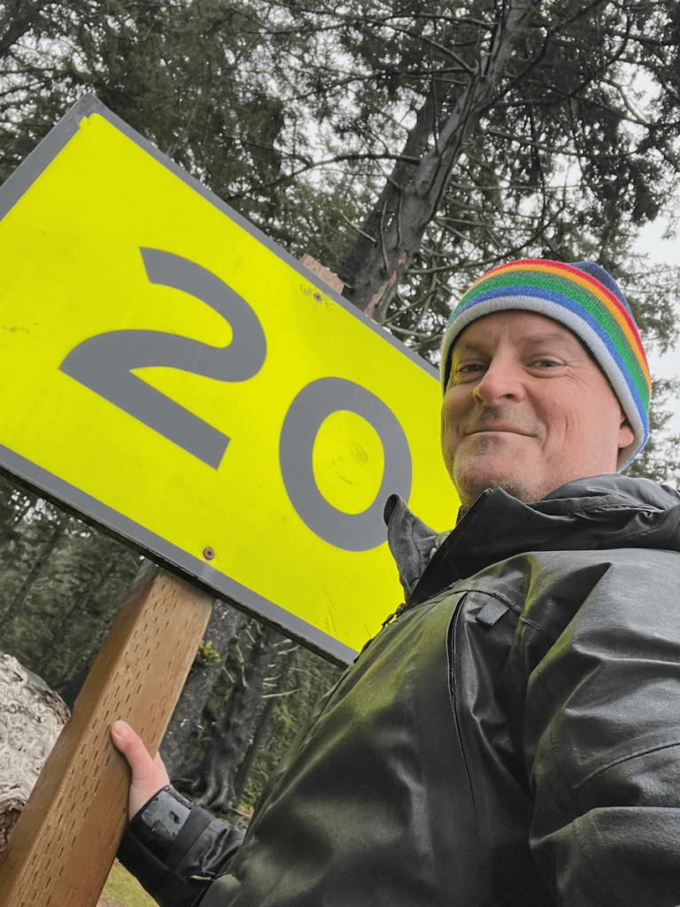 Matthew Kessi poses for a selfie in front of a yellow sign with a large black number 20 which is the safety location for Oswald West State Park on the Oregon Coast.