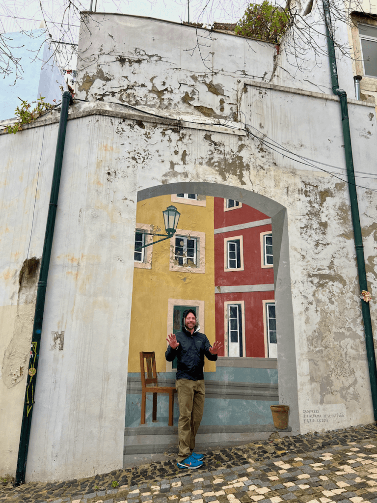 A man stands against a mural on a walking tour of Lisbon Portugal. He looks like he's in a courtyard but it is an optical illusion.