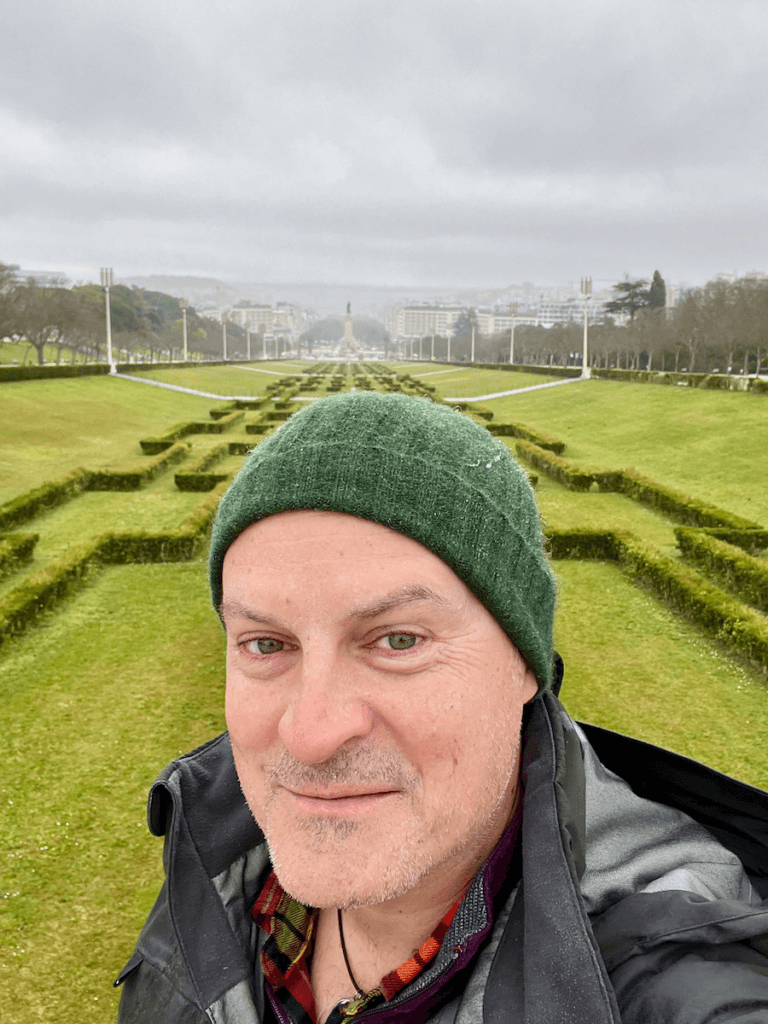 Matthew Kessi poses for a selfie in front of a grand formal lawn in Lisbon Portugal. In the background can be seen a statue rising up in a ceremonial roundabout on the main avenue.