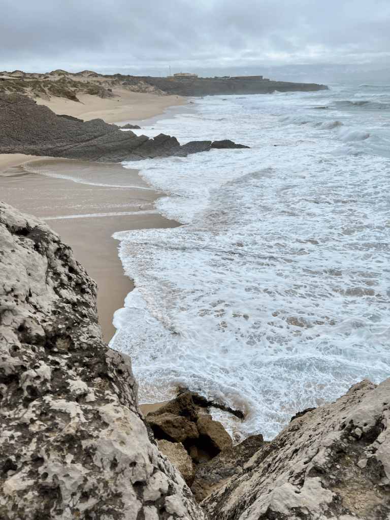 The Atlantic coast of Portugal makes for a great nature forward experience. Here the frothy waves crash against worn down lava rocks with cloudy skies above.