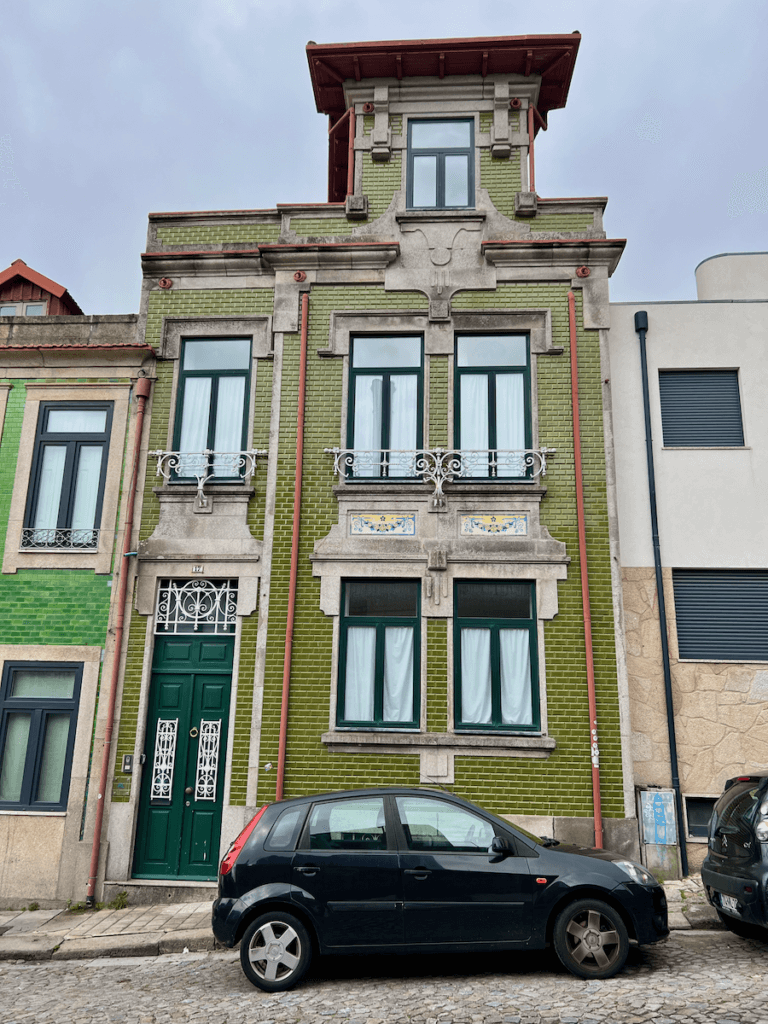 A traditional brick building in Porto Portugal with green tile and a car parked on the cobblestone street below.