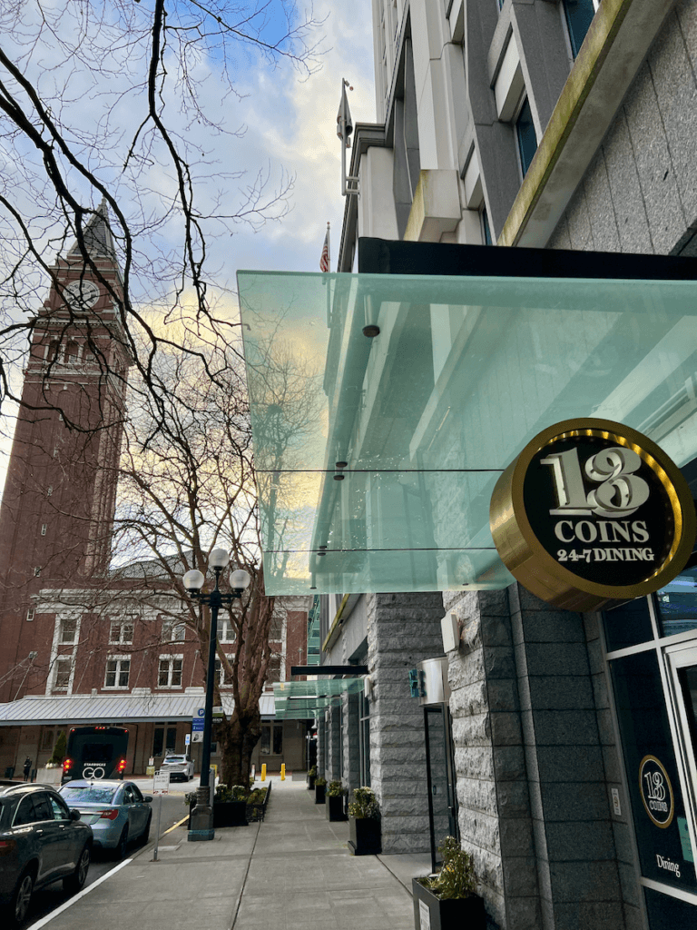 Seattle's King Street Station steeple rises up above the street in Old Town Seattle. The sign for 13 Coins restaurant in is the foreground.