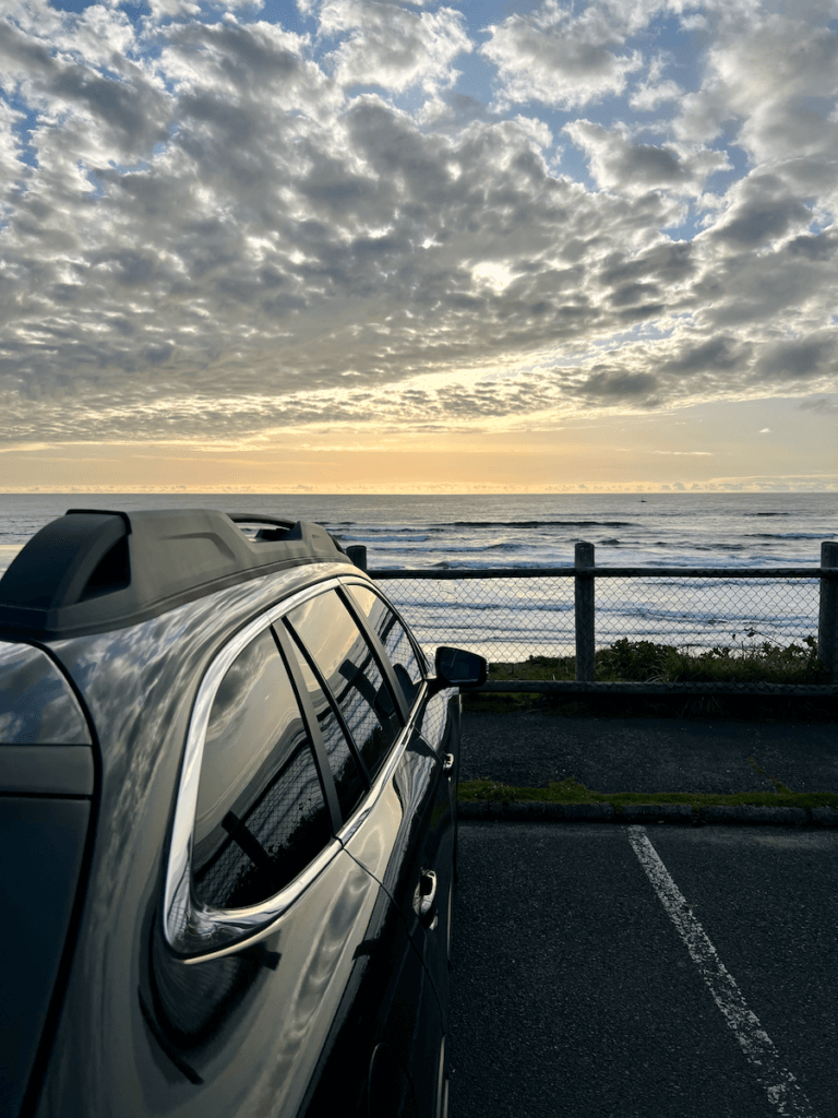 A Subaru sits parked overlooking the surf of the Oregon Coast at sunset.