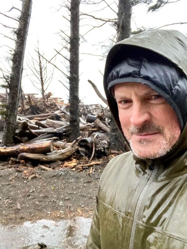 Matthew Kessi is soaking wet on Rialto Beach on the Olympic Peninsula. It's winter and he's wearing a green jacket and peering through a hood.