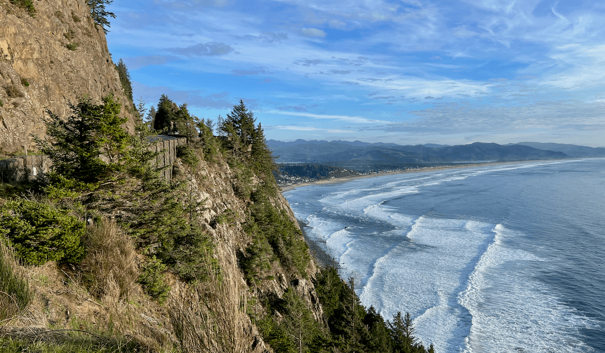 Waves of the Pacific Ocean flow into a beach on the Oregon Coast. This perch is high up on a mountain with cliffs of jagged rock flowing.