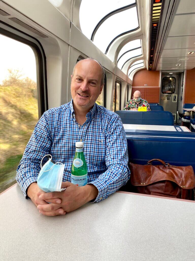 Matthew Kessi smiles while seated on the dome sightseeing car on the Coast Starlight train, which goes from Seattle to Los Angeles. He's holding a bottle of pelligrino. 