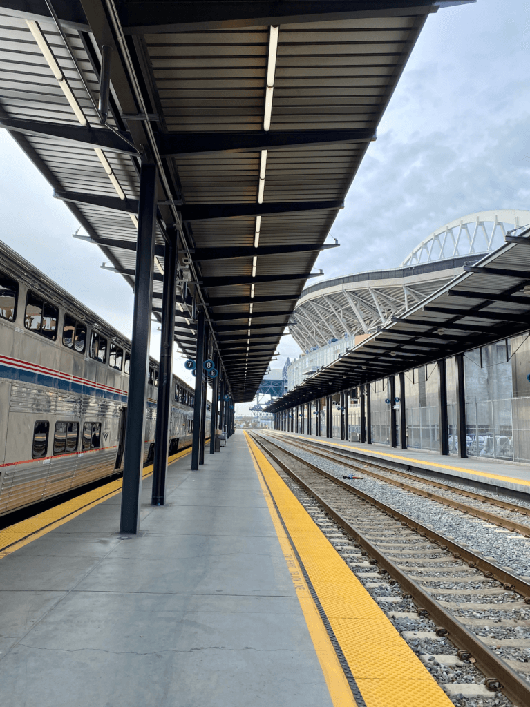 Kind Street Station in Seattle has a double decker Amtrak train and several other vacant tracks of the platform. Qwest Field is rising up from behind the station. 