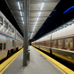 Amtrak operates two kinds of trainsets on the Seattle to Portland train, as shown in this photo. On the left is a double-decker long haul train, with shiny silver siding with blue and red stripes and on the other side is a one-level glossy train with brown and green striping. This photo is taken at the Seattle train station at night.