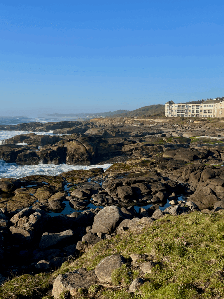 The Overleaf Lodge in Yachats Oregon overlooks the stunning rugged beauty of waves crashing on rocks, under a blue sky.